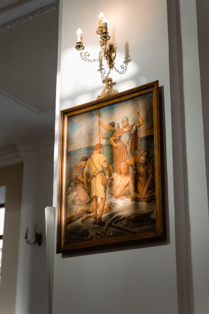 Vertical shot of a historic painting and ornate chandelier on a church wall.